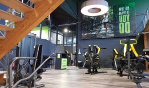Offener Trainingsbereich im EASYFITNESS-Studio mit Kraftgeräten, Holztreppe und grünen Markenelementen
