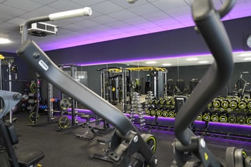 Krafttrainingsbereich mit modernen Fitnessgeräten, Kurzhanteln und violetter Beleuchtung