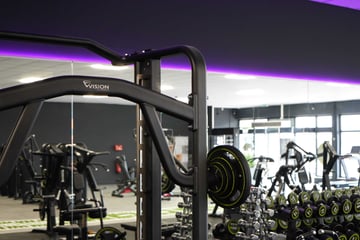 Krafttrainingsbereich im EASYFITNESS-Studio mit Langhantelstation, Kurzhanteln und violetter Beleuchtung