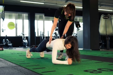Trainerin unterstützt eine Frau beim Unterarmstütz auf der Functional-Training-Fläche im EASYFITNESS-Studio