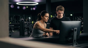 Mitarbeiterin zeigt einem Kollegen die digitale Studioverwaltung am Computer im EASYFITNESS-Studio