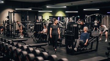 Belebter Trainingsbereich im EASYFITNESS-Studio mit Mitgliedern und Trainer an verschiedenen Kraftgeräten